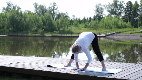 A Relaxed Athletic Mature Woman Does Yoga in the Park Near the Lake