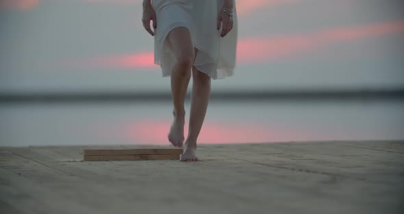 Blonde Woman in White Dress is Walking on the Pier of the Lake and Tensing Up