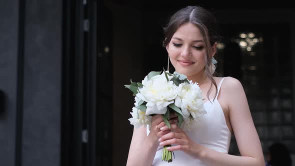 Beautiful Bride in a White Dress Sniffs a Wedding Bouquet on the Background of the Church