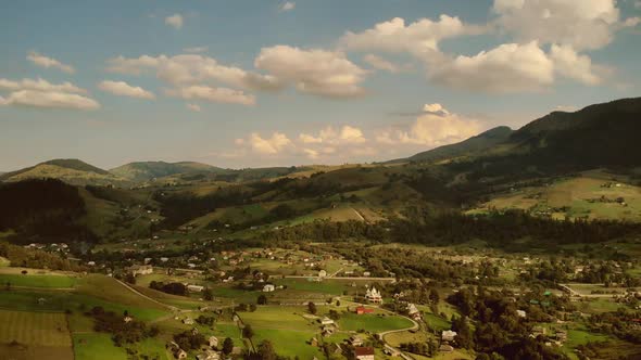 Mountain Landscape with Hills Forests Houses Fields and Cloudy Sky