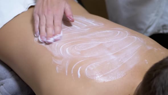 Hands of the Masseur are Massaging Back a Child Using Cream