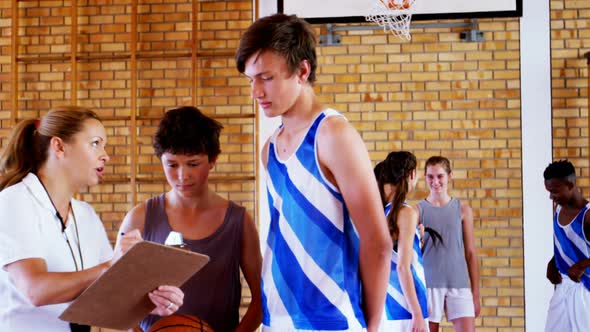 Female coach instructing schoolboys in basketball court