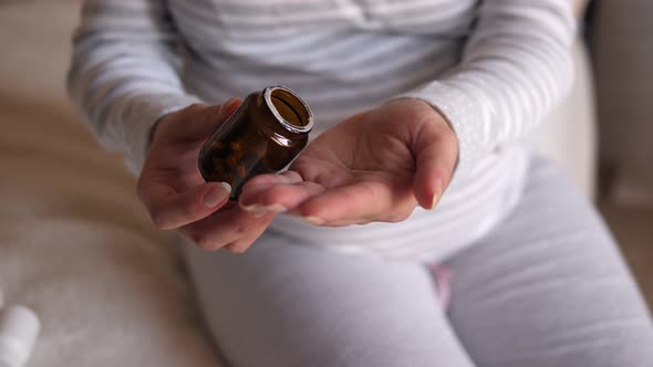 A Pregnant Woman Sits on the Bed and Pours Pills Into Her Hand. Close-up.
