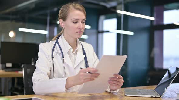 Hardworking Young Female Doctor Reading Documents in Office