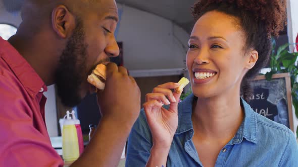 Close up of african american couple eating burgers and fries together at the food truck