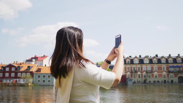 Back view of Asian woman standing and taking a photo of beautiful buildings by a river view