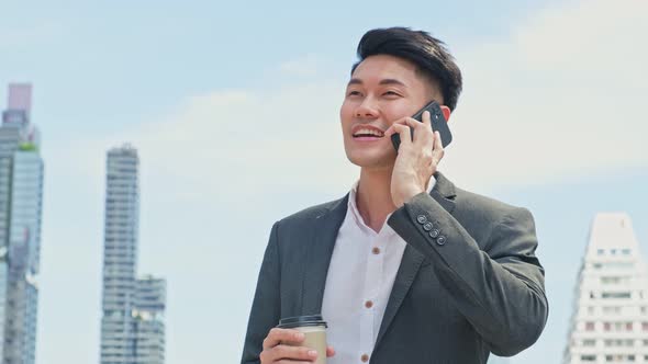 Asian young smart business man holding a cup of coffee and talking in telephone while walk in city.