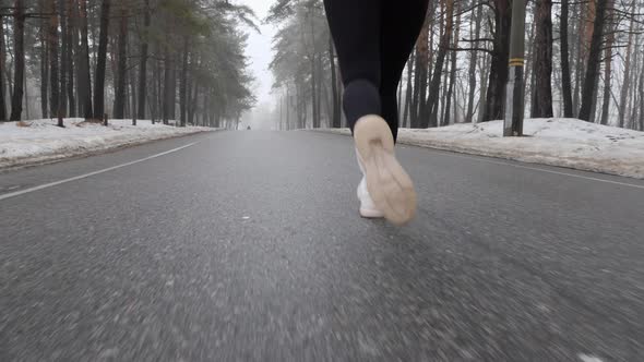 Legs of Young Attractive Caucasian Girl Running in The Snowy Park in Winter with Headphones