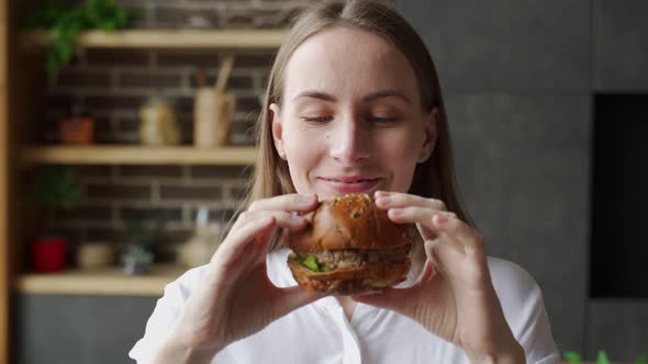 Hungry Woman Eating a Hamburger Sitting in the Kitchen