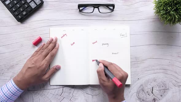 High Angle View of Man Hand Writing on Weekly Planner on Table. alt