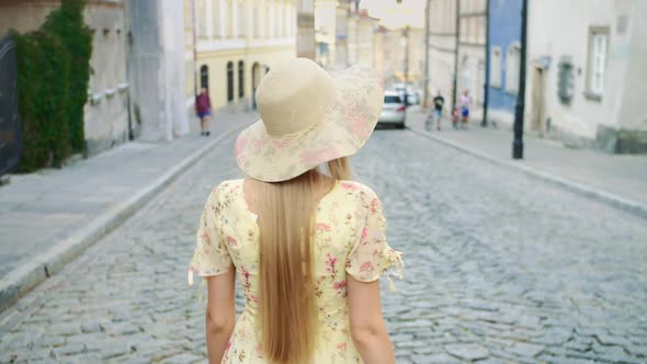 Smiling Woman Walking on Street. Cheerful Pretty Girl in White Hat Looking Back at Camera While