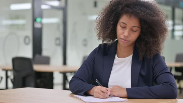 Serious Young African Businesswoman Writing on Paper 