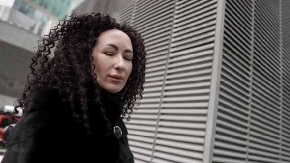 Eccentric Brunette Woman with Long Curly Hair Is Posing for Camera on City Street