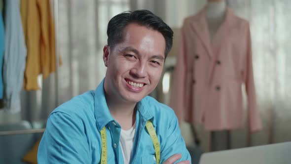 Asian Male Designer Working On A Laptop And Smiling To The Camera With Arms Crossed While Designing