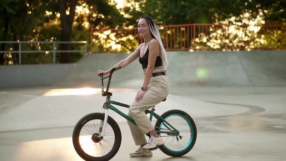 Portrait of a Beautiful Girl with Black and White Dreadlocks Sitting on the Bike in Skate Park and