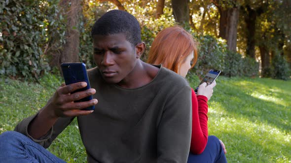 Youth,technology,devices.Mixed lfriends using smartphones sitting on the grass