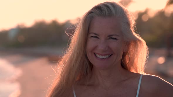 Portrait of beautiful backlit mature woman flipping her hair across her head while on a tropical bea