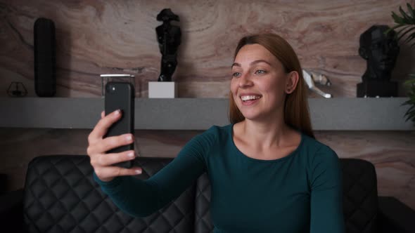 Young Woman Having Video Chat Using Smartphone at Home Waving Hand 