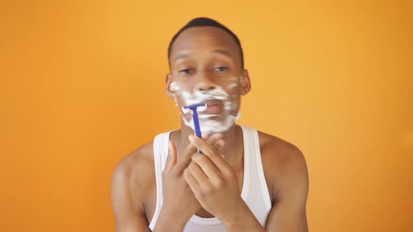 Young African American Man Posing for the Camera on a Yellow Background, He Shaves with Foam 