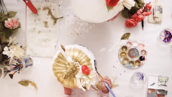 Top view. Mother and daughter painting face of an unicorn and decorating craft pumpkins with flowers