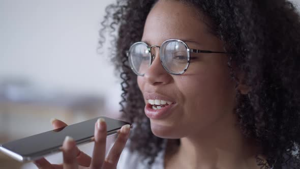 Closeup of Cheerful Young Beautiful African American Woman in Eyeglasses Recording Voice Message on