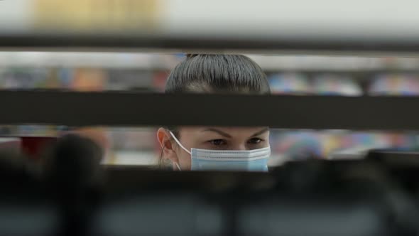 Young Woman in a Protective Mask Is Choosing Something on the Shelves in the Store