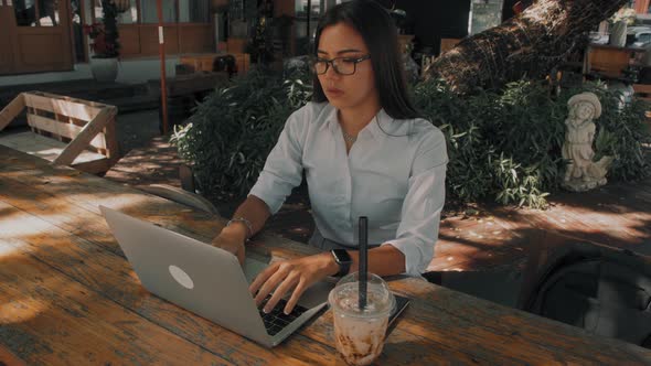 Asian Attractive Young Woman Wearing Glasses Working at Her Laptop on the Street