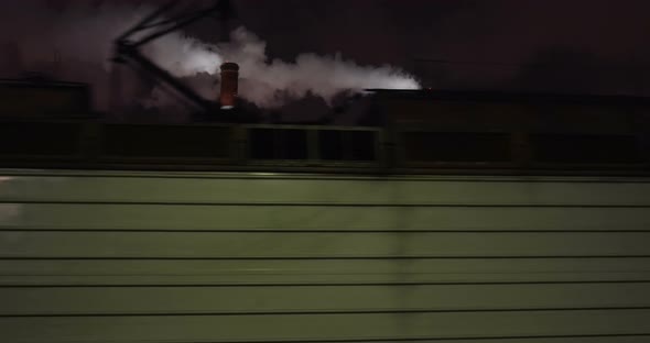 Passenger train passing by factory at night