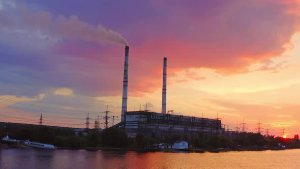 Industrial area at sunset. Factory near the river on the beautiful pink sky.