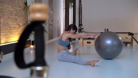 Flexible woman warming up legs with fit ball during training