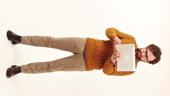 Young Attractive Bearded Caucasian Man Stands Working with His Laptop Focuses on the Screen Hipster