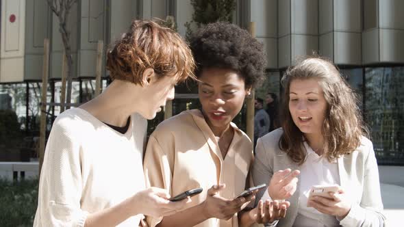 Three Women with Smartphones Sitting on Street