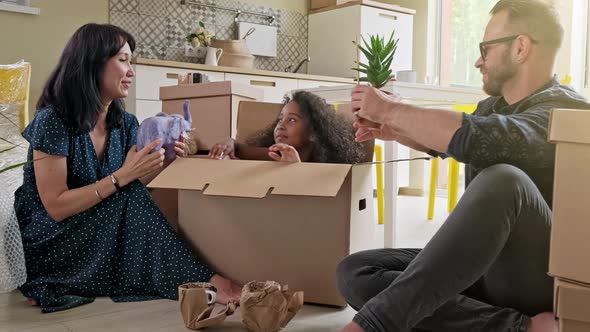 Happy Mixed Ethnicity Smiling Family with Small Son and Daughter Unpacking Boxes Together Sitting on