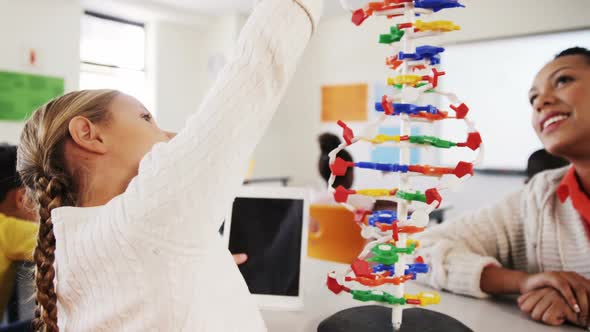 Teacher assisting schoolgirl with molecule model in classroom