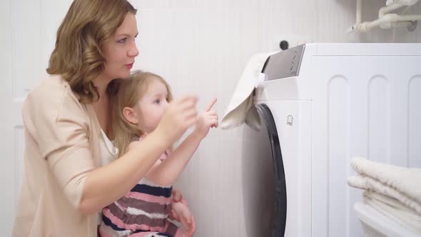 Mom and Little Girl Close the Washing Machine Door and Turn It on