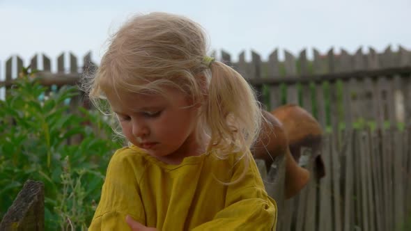 Tanned Blond Farm Girl is Standing on the Background of an Old Village Fence