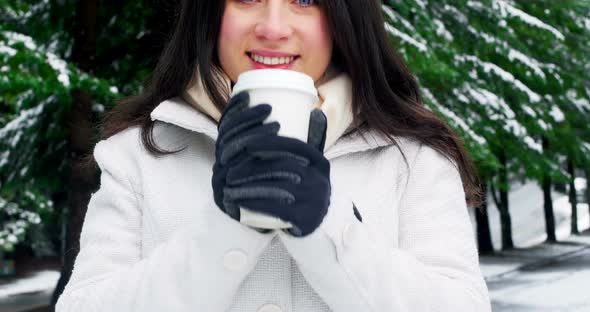 Smiling woman in warm clothing having coffee during snowfall