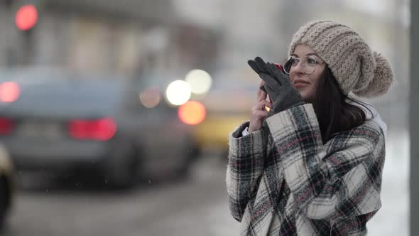 Young Cheerful Woman Is Talking on Speakerphone in Cell Phone Outdoors at Winter Day