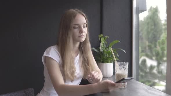 A woman communicates using messages on the phone while in a cafe and drinks a cocktail