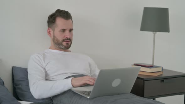 Man Celebrating Success on Laptop in Bed