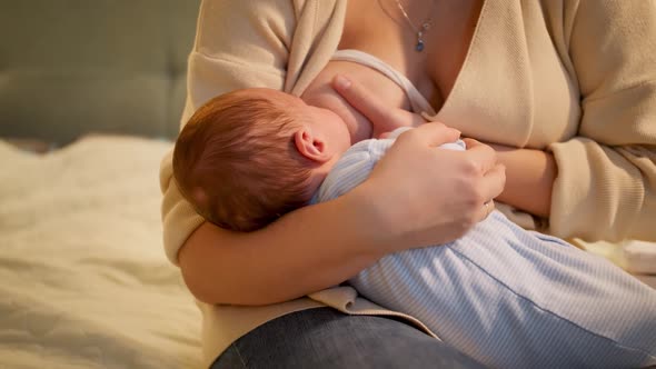 Cute Little Newborn Baby Sucking Milk From Mothers Breast Sitting on at Night