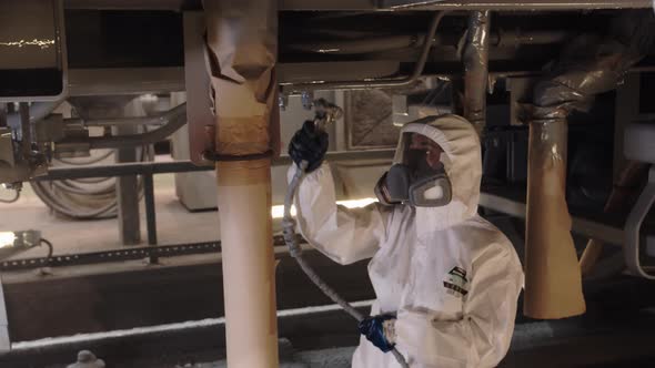 A Woman Molar Paints the Metal Structure of a Car in a Hardtoreach Place with Gray Paint From a