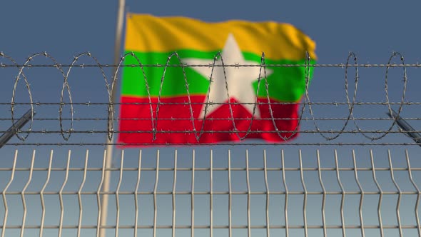 Waving Flag of Myanmar Behind Barbed Wire Fence