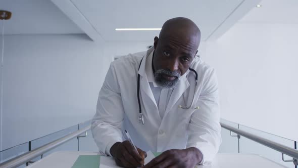 Portrait of african american male senior doctor taking notes while looking at the camera at hospital
