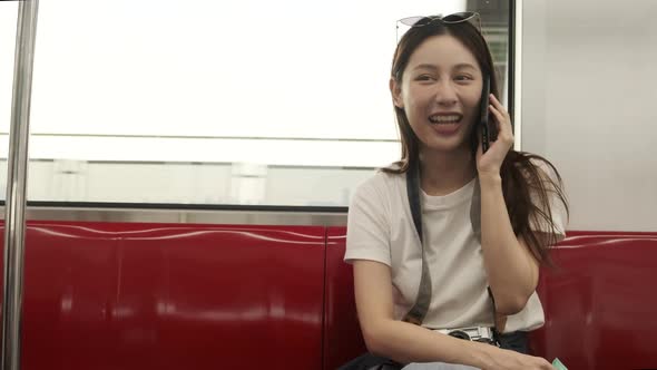 Asian female tourist talking mobile phone, transporting in urban view by train.