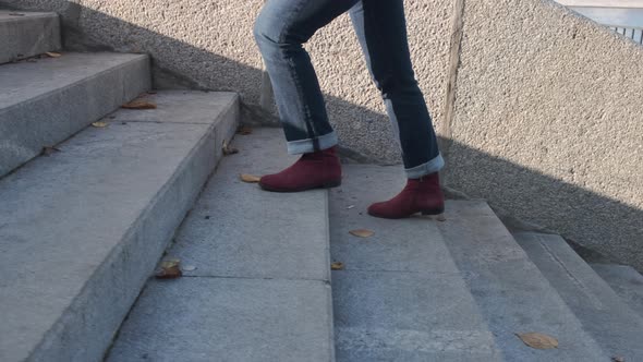 Female Legs in Burgundy Boots and Blue Jeans Climb the Stone Stairs