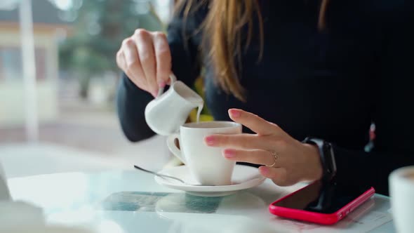 Woman pouring milk into coffee cup on the table.