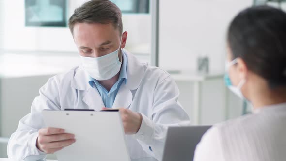 Male Physician in Protective Mask Speaking with Woman in Medical Office