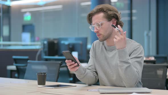 Young Businessman with Pen Using Smartphone in Office