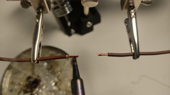 Electrician with a soldering iron solders electric cables with tin